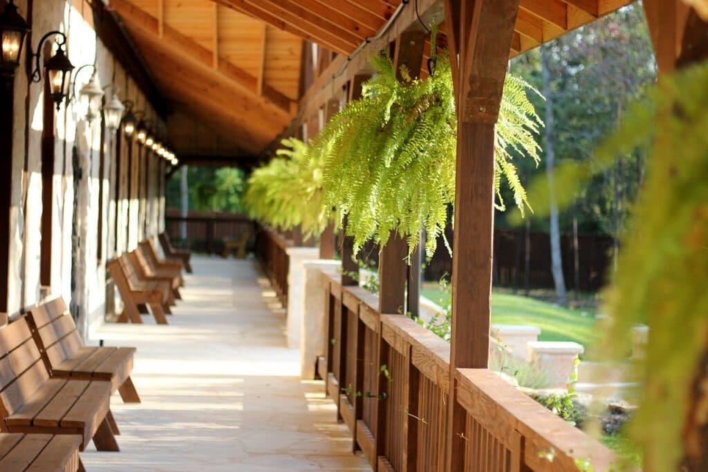 A covered wooden porch lined with benches and hanging ferns